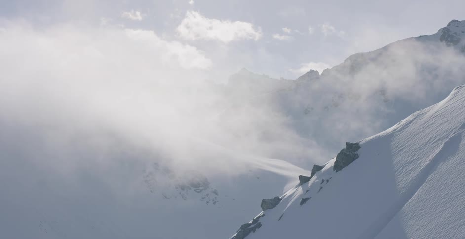 Clouds roll over snowy mountains with sun shining behind