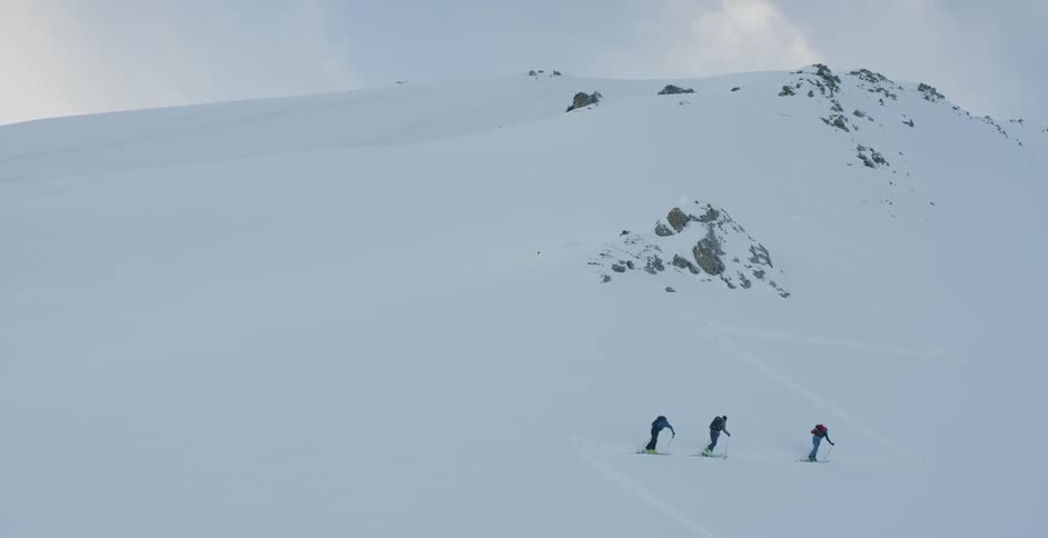 Three people ski tour up a snowy mountain