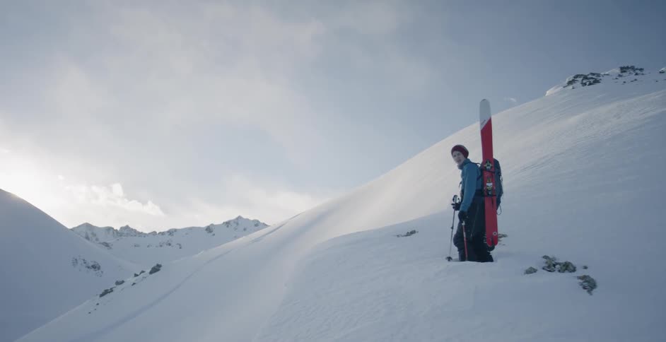 a skier points with his ski pole atop a snowy mountain