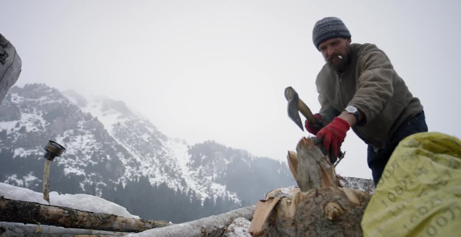 A man cuts a log with an ax while it snows