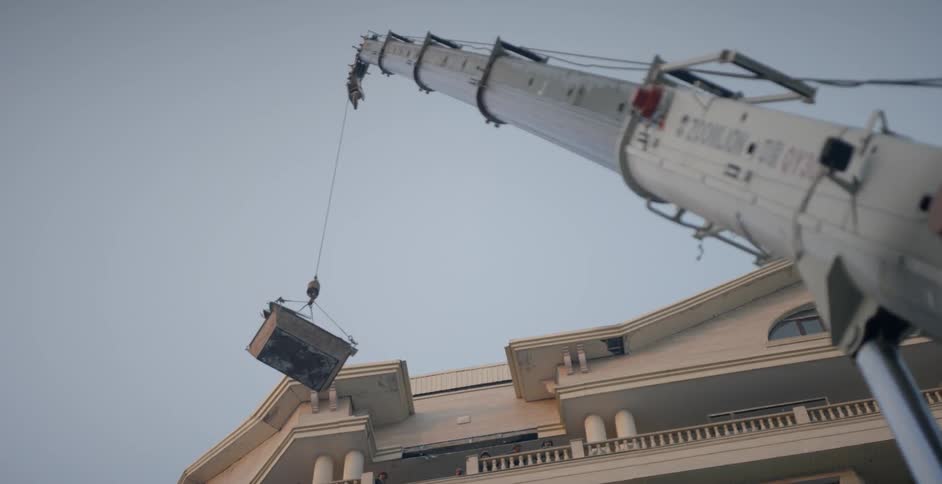 Large crane moves a container away from a building top