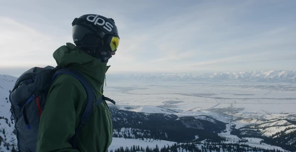 A skier looks out from atop a snowy mountain