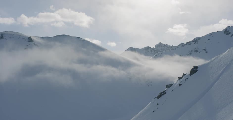Clouds pass through and above tall snow covered mountains