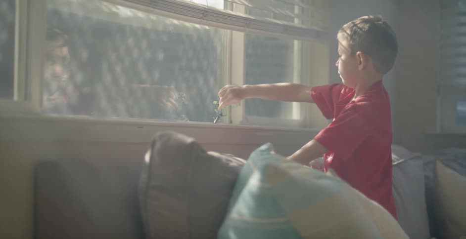 A young boy plays with a toy on a window sill