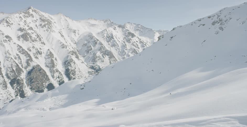 A person skis at the foot of large mountain covered in snow
