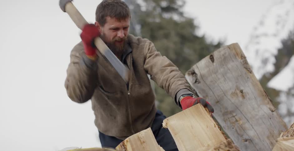 Bearded man chops wood with an ax