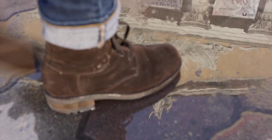 A person wearing boots walks through a puddle