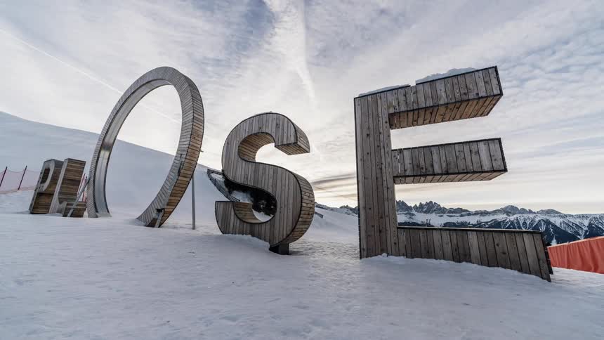 Large wooden letters sit in the snow as clouds go by