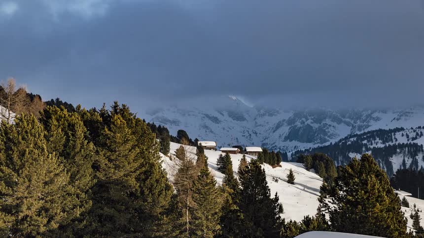 Clouds pass above a forest and snow covered mountains