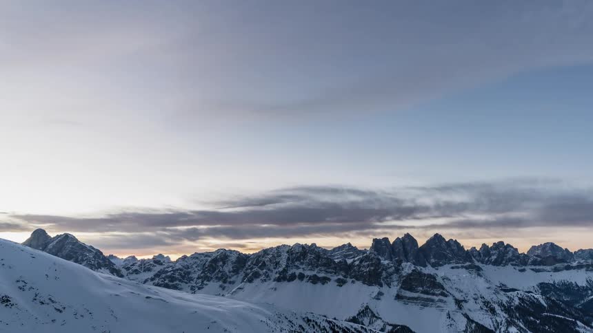 Clouds are moving across snow-covered mountains at dusk