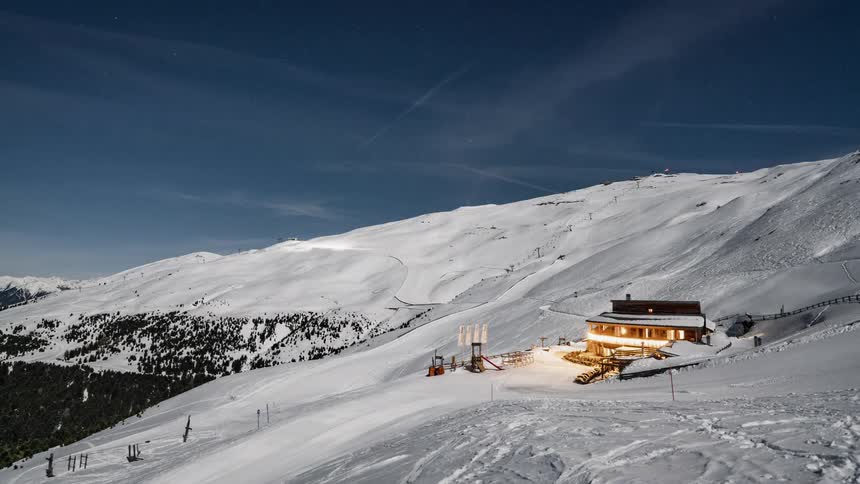 A cabin is illuminated on the side of a snowy mountain