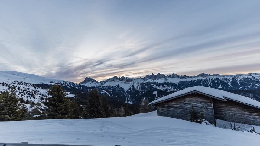 The sun rises over snow covered peaks and a cabin