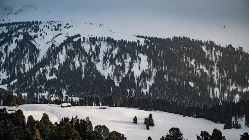 Snow is covering a cabin in a mountain region during the day