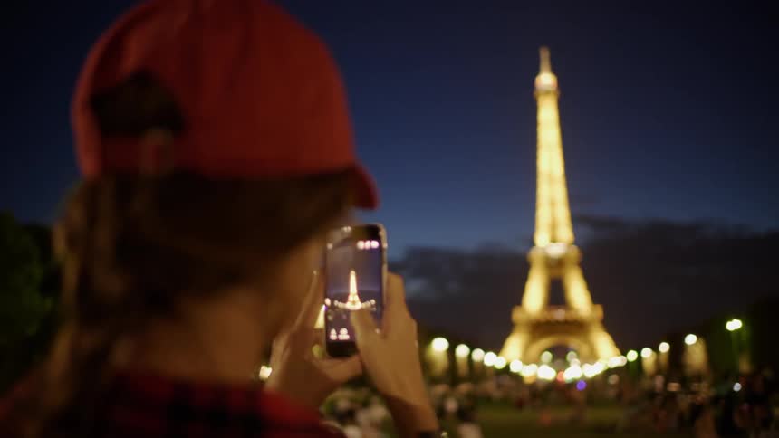 A woman photographs the eiffel tower at night