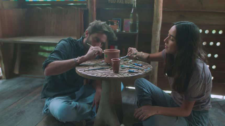 Man and woman sit on the floor as they paint a piece of pottery