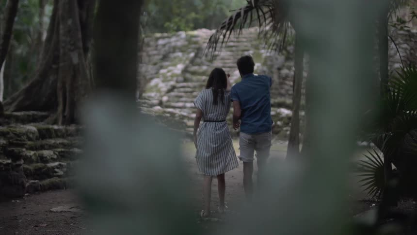 A man and woman walk towards ruins in a jungle