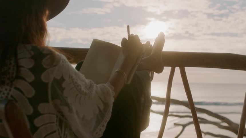 Woman draws in a notebook as she sits near a railing