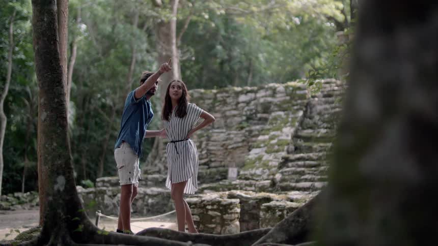 A man and woman look at ruins in a forest