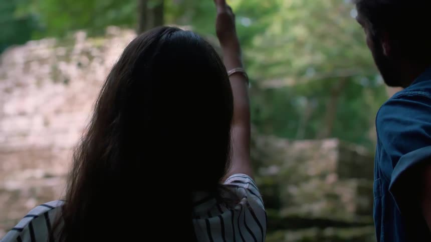 A man and woman talk outside a stone structure in the woods