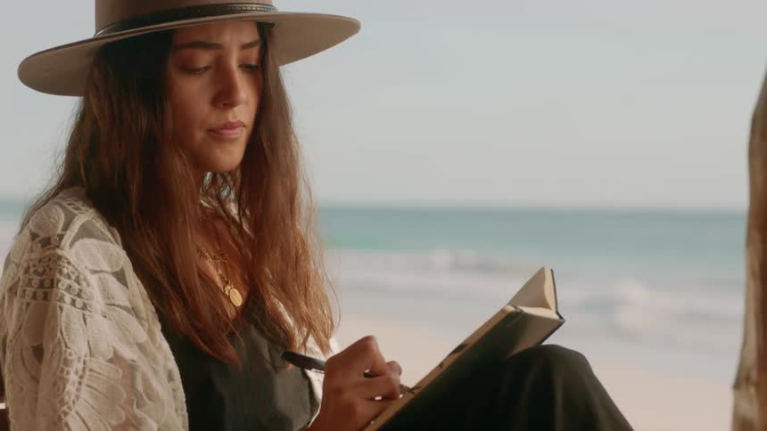 A woman writes in a notebook on a beach