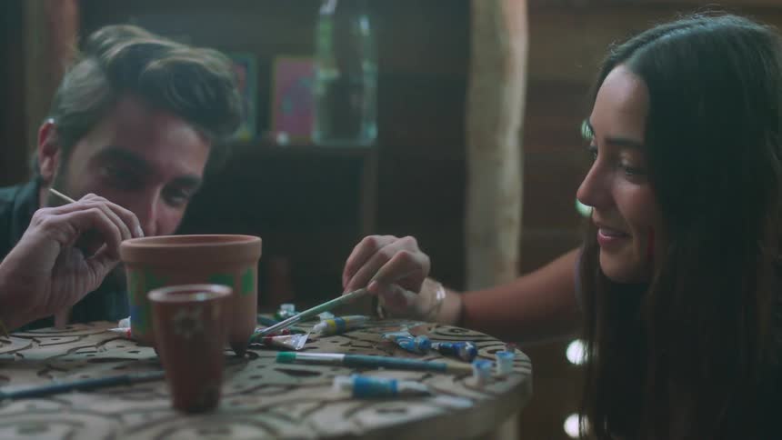Man and woman smile as they paint a pottery piece