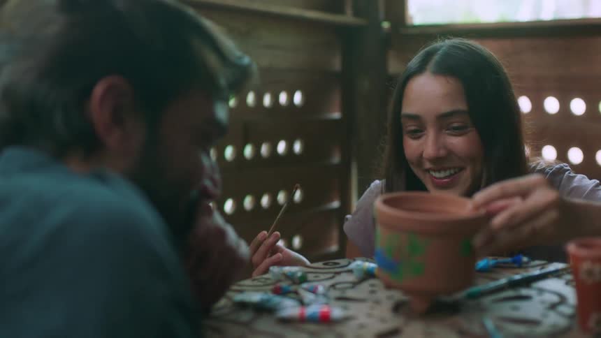 A man and woman laugh while painting pottery