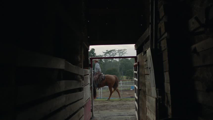 Cowboys are riding horses past a stable in daylight