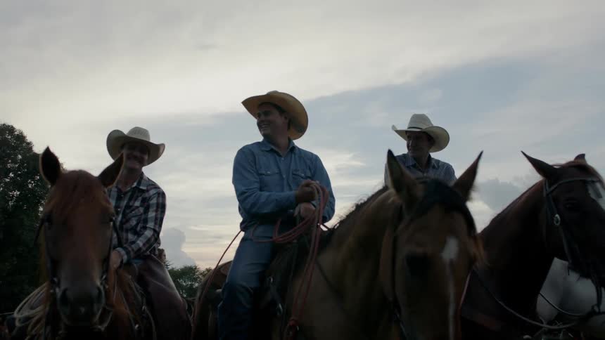 The cowboys are laughing and talking while sitting on their horses