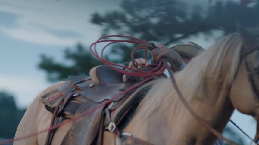 Cowboy dismounting his horse as he wraps a rope around the saddle horn