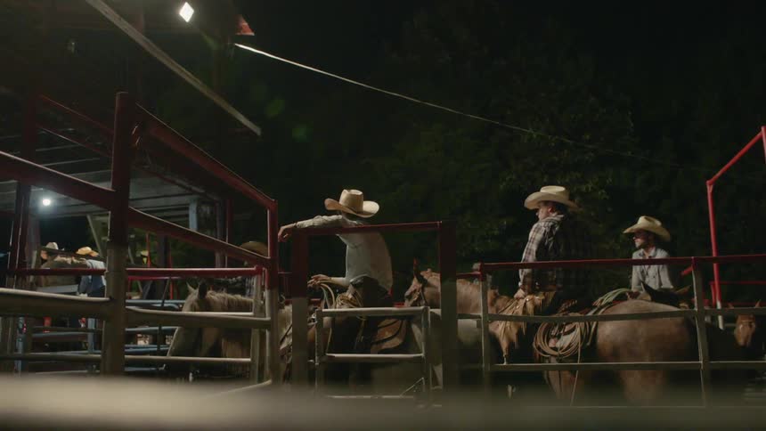 Cowboys sit on horses in a pen at night