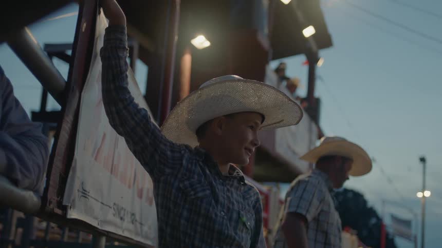 Child wearing a cowboy hat holds onto a gate