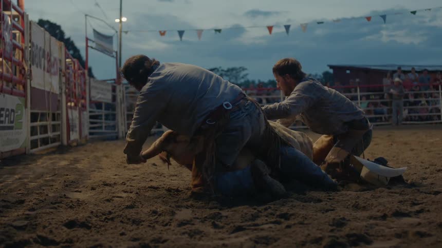 Two men wrestle a bull to the ground in a corral
