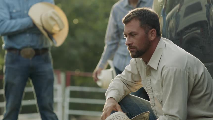 A cowboy is crouched next to a truck