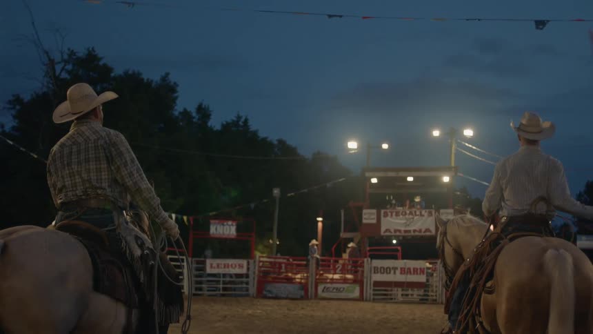 Two men ride on top of horses in a rodeo arena