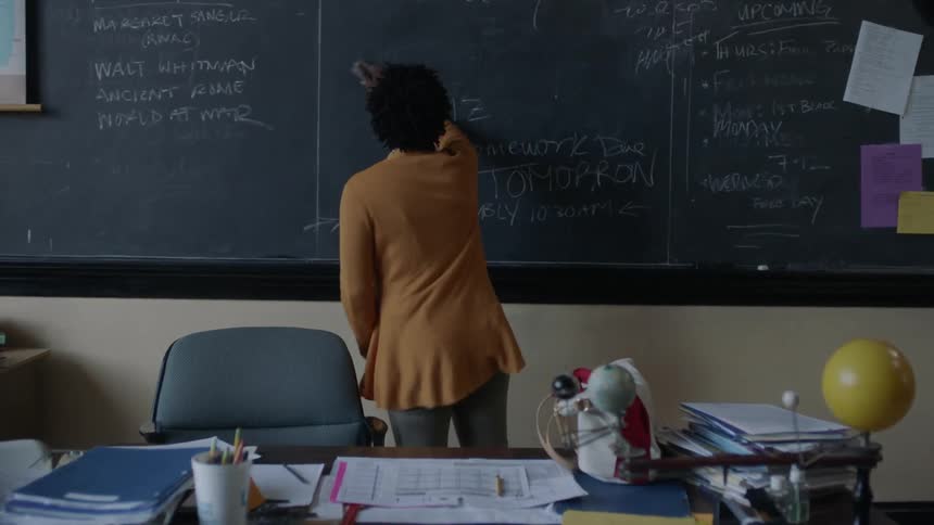An upset teacher erases writing from a chalkboard