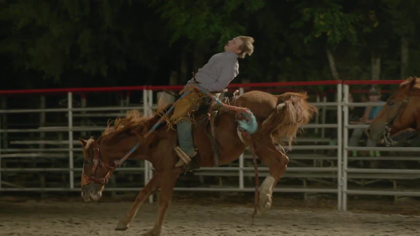 Man rides a bucking horse in a corral