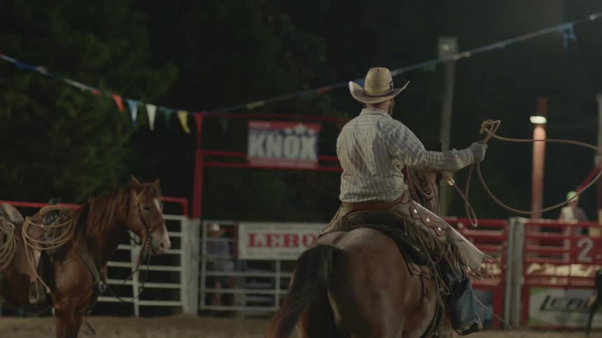 Man holding a rope rides a horse in a corral