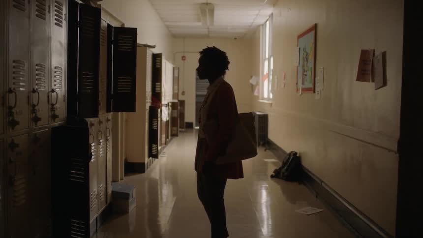 Woman standing in a school hallway staring at lockers and some of them are opened