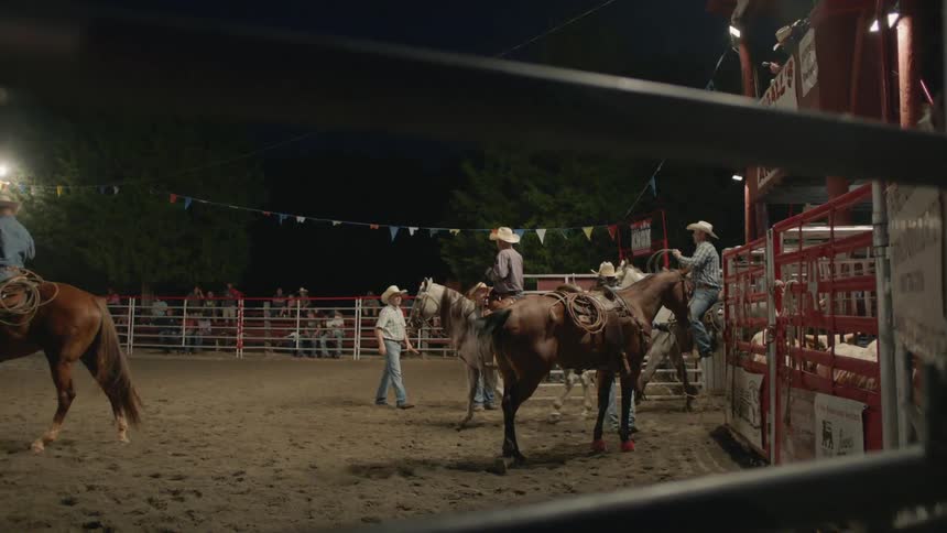 Several people ride horses in a ring with an audience watching