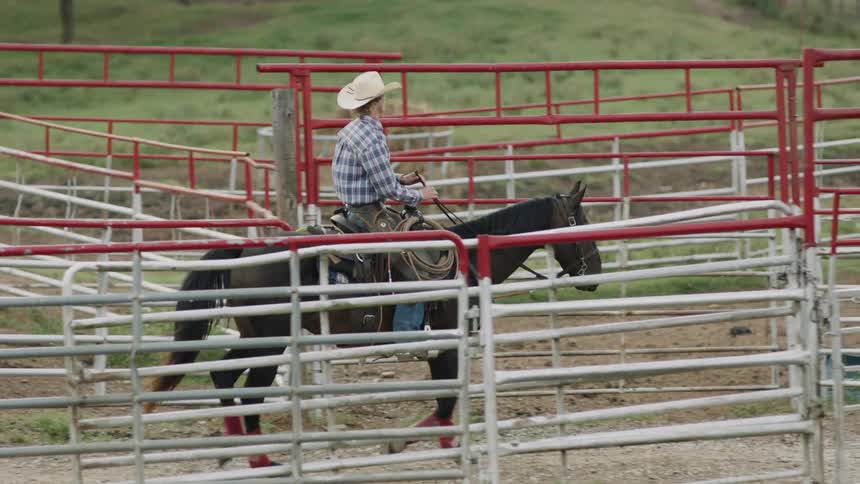 Cowboy rides a horse on a fenced path