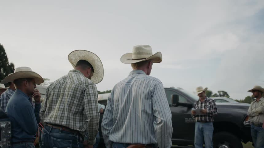 A man is reading instructions to a group of cowboys outside during the day