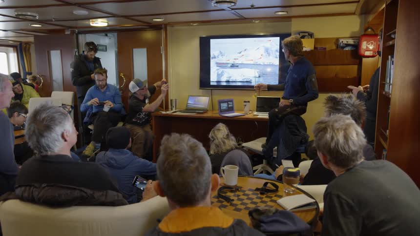 Group of people sit at tables watching a television