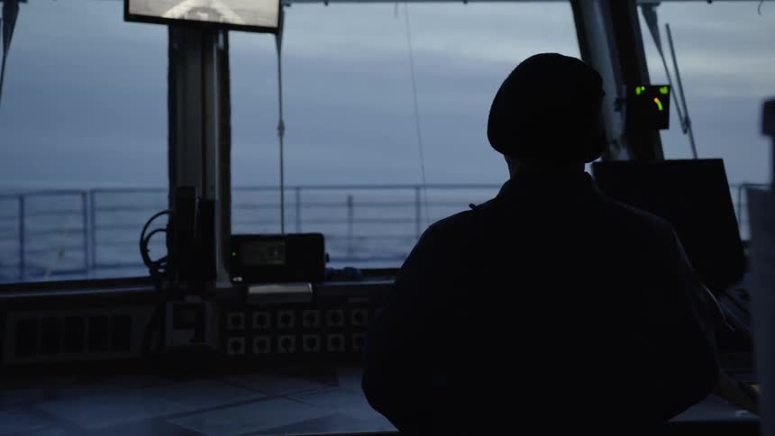The ship captain standing watch as it sails through the ocean on a cloudy evening