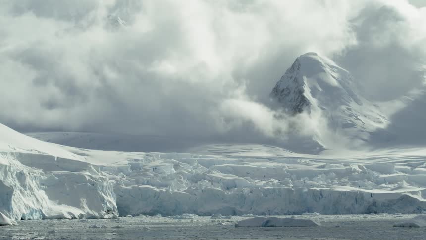 Clouds hang above the snow covered glacier crashing into ocean below