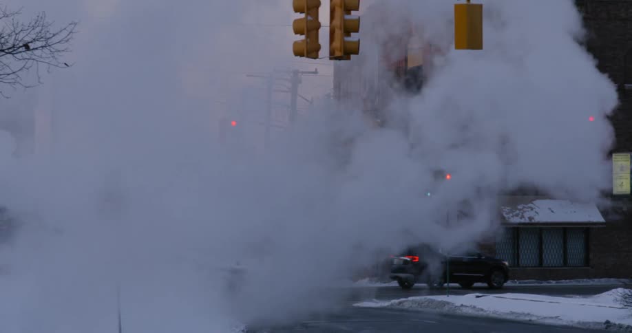 Steam floats down a city street at sunset