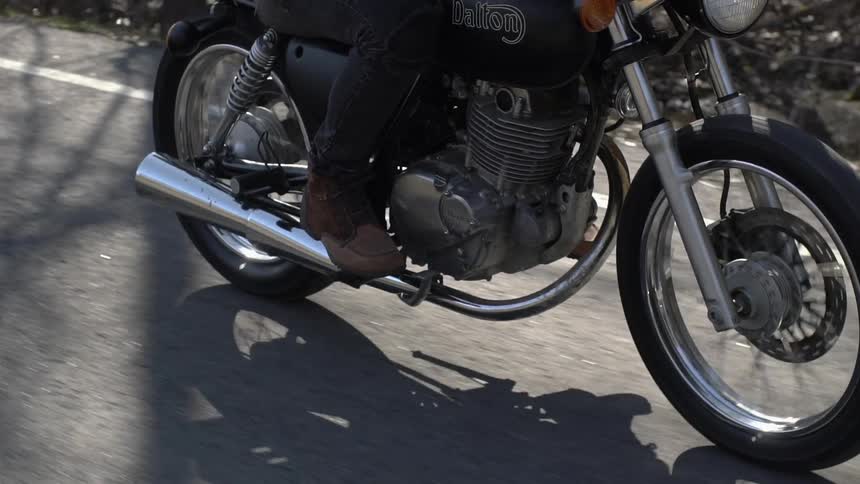 A person is riding a motorcycle on a road near a stream in daylight