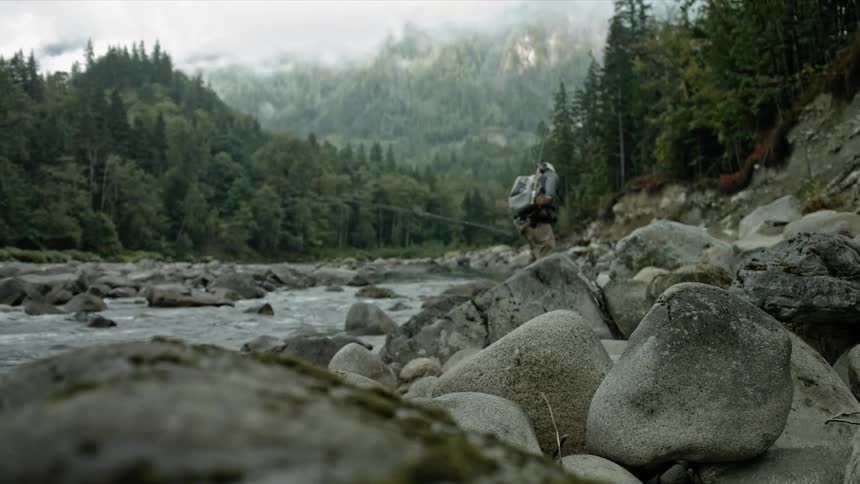 Fisherman walking on some large rocks lining a river on a cloudy day