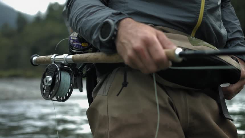 Man holds a fly fishing rod as he stands in a creek
