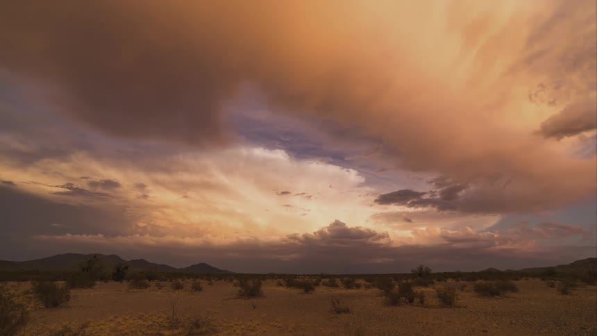 A timelapse view of clouds rolling over the desert, changing colors from white, brown, pink, and then night falls