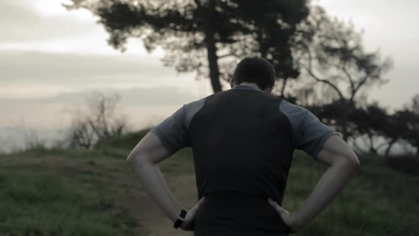 Man wearing ear buds jogs through the forest and out onto a field
